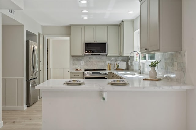kitchen with a peninsula, light wood-type flooring, gray cabinets, a sink, and stainless steel appliances