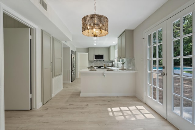 kitchen with decorative backsplash, light wood-type flooring, a sink, a chandelier, and stainless steel appliances