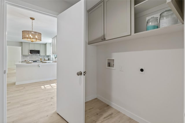 laundry area featuring an inviting chandelier, hookup for a washing machine, cabinet space, light wood finished floors, and hookup for an electric dryer