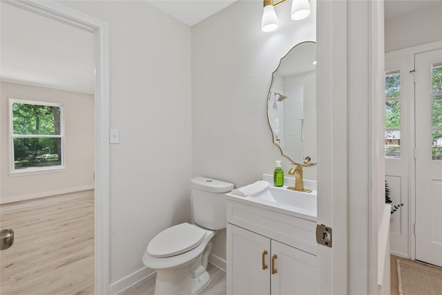 bathroom with baseboards, plenty of natural light, toilet, and wood finished floors