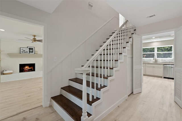 stairs featuring ceiling fan, visible vents, wood finished floors, and a fireplace