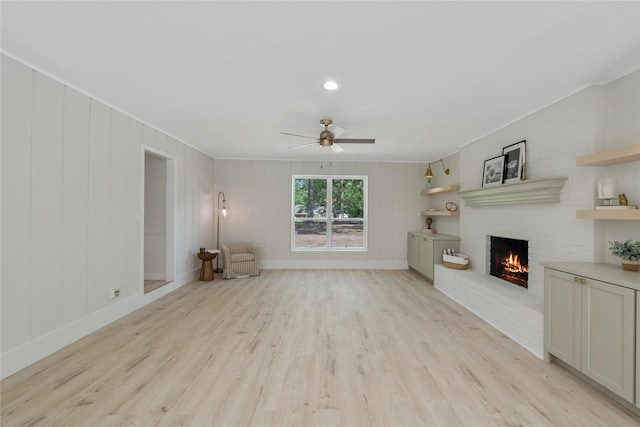 unfurnished living room featuring crown molding, a ceiling fan, light wood-style flooring, and a fireplace