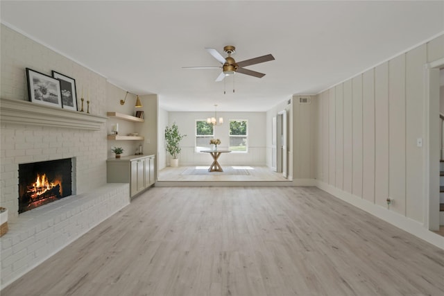 unfurnished living room featuring stairs, light wood-style flooring, ceiling fan with notable chandelier, and a fireplace