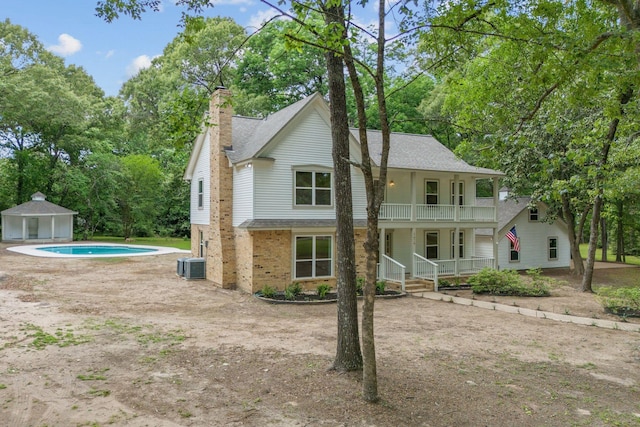 back of property featuring a porch, an outdoor pool, a chimney, a balcony, and central air condition unit