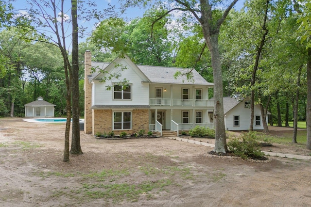 view of front facade featuring a balcony, covered porch, an outdoor pool, a chimney, and an outbuilding