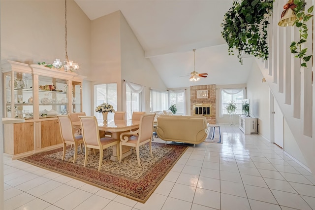 dining space with baseboards, ceiling fan with notable chandelier, a brick fireplace, high vaulted ceiling, and light tile patterned floors