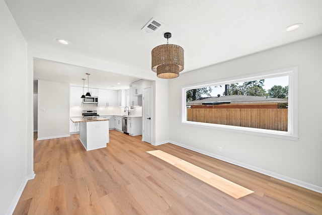 4207 Marlborough Dr, Houston, TX 77092 - kitchen featuring stainless steel appliances, white cabinets, a kitchen island, light wood-style flooring, and baseboards