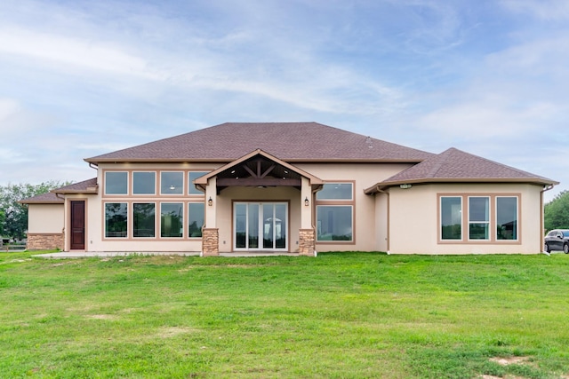 rear view of house with stucco siding, roof with shingles, and a yard