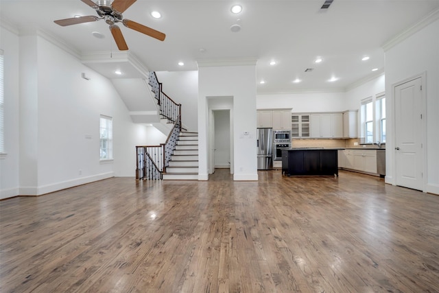 living area featuring recessed lighting, a ceiling fan, wood finished floors, ornamental molding, and stairway