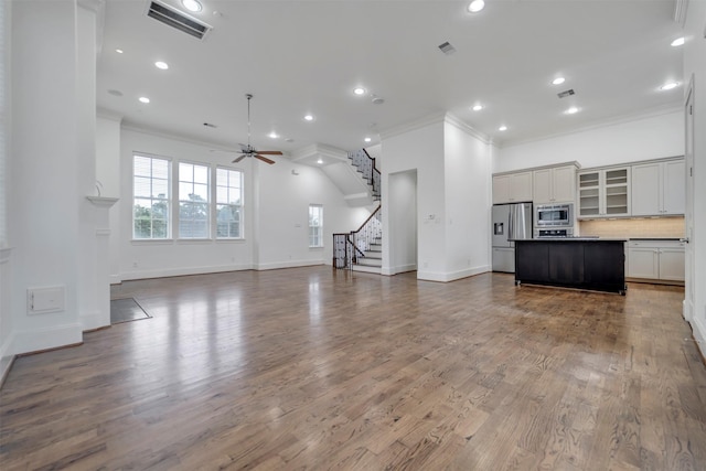 unfurnished living room featuring ceiling fan, stairs, baseboards, visible vents, and ornamental molding