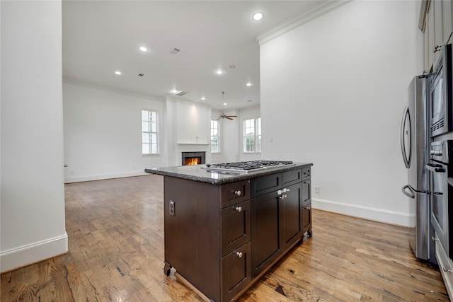 kitchen featuring dark brown cabinets, baseboards, a warm lit fireplace, ornamental molding, and stainless steel appliances