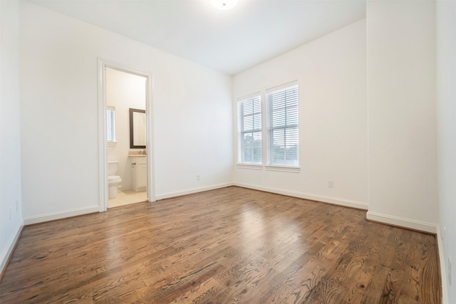 unfurnished bedroom featuring baseboards, wood finished floors, and ensuite bath