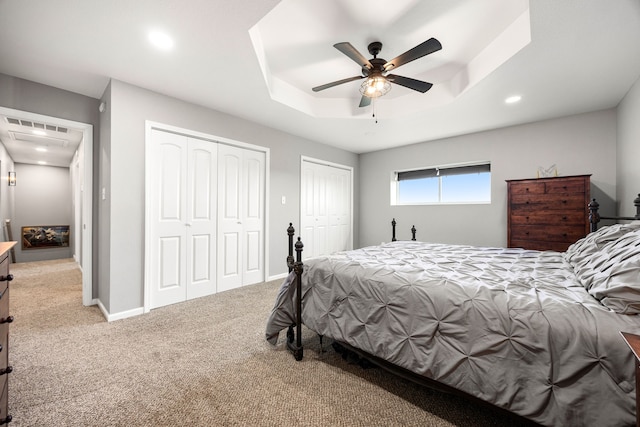 carpeted bedroom featuring a ceiling fan, multiple closets, a tray ceiling, baseboards, and recessed lighting