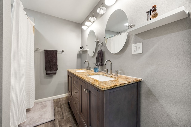 full bath featuring double vanity, wood finished floors, baseboards, and a sink