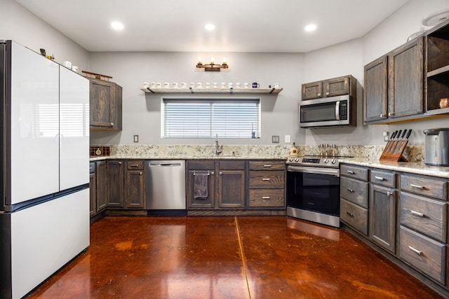 kitchen featuring stainless steel appliances, a sink, dark brown cabinetry, concrete flooring, and light stone counters