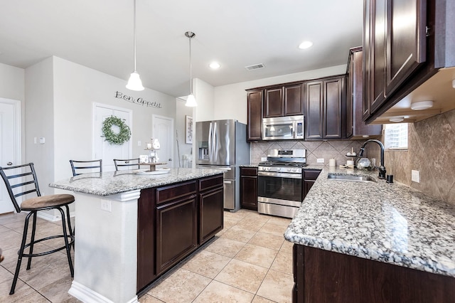 3901 Penny Ln, Deer Park, TX 77536 - kitchen featuring appliances with stainless steel finishes, a sink, light tile patterned floors, dark brown cabinetry, and a kitchen island