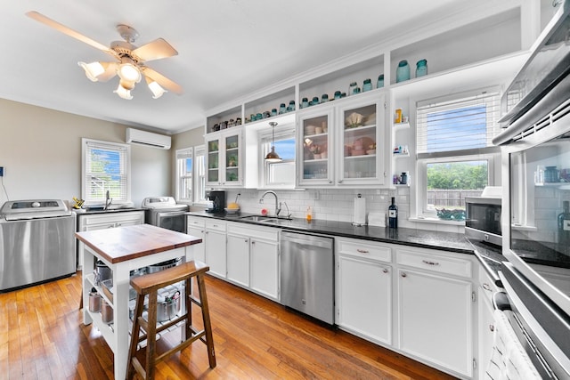 kitchen with a sink, backsplash, a wall mounted air conditioner, appliances with stainless steel finishes, and washer / dryer