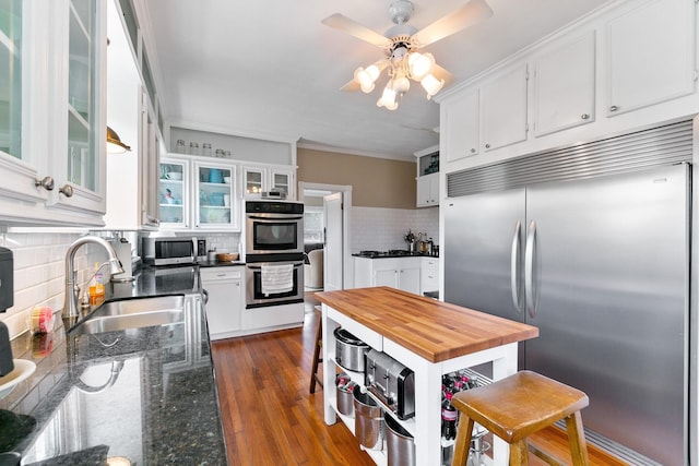 kitchen featuring stainless steel appliances, a sink, butcher block counters, decorative backsplash, and white cabinetry