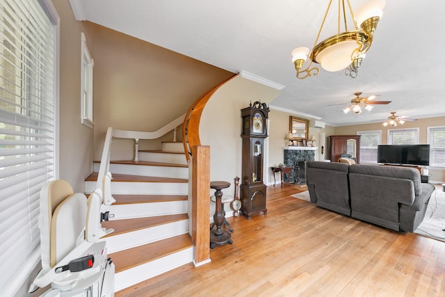 living room featuring ceiling fan with notable chandelier, wood finished floors, a fireplace, and ornamental molding