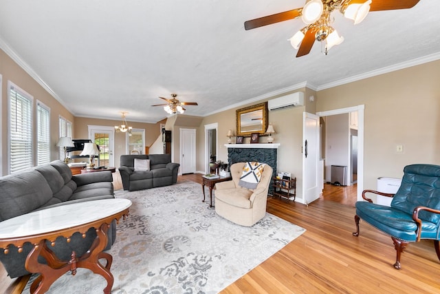 living area with a wall mounted air conditioner, a stone fireplace, wood finished floors, ceiling fan with notable chandelier, and baseboards