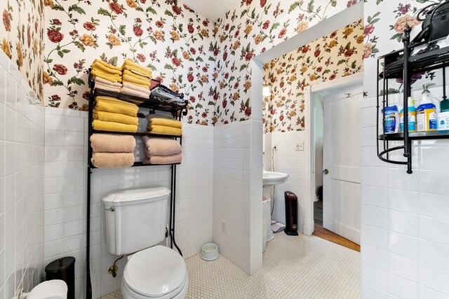 bathroom with wainscoting, toilet, wallpapered walls, and tile walls