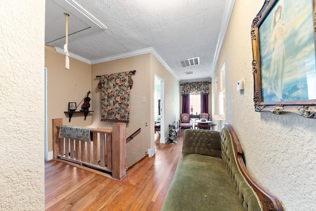 hallway with a textured ceiling, wood finished floors, visible vents, and a textured wall