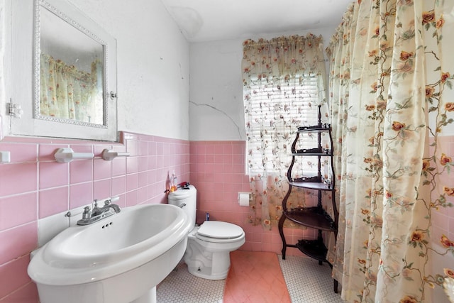 bathroom with tile walls, a wainscoted wall, a sink, and toilet
