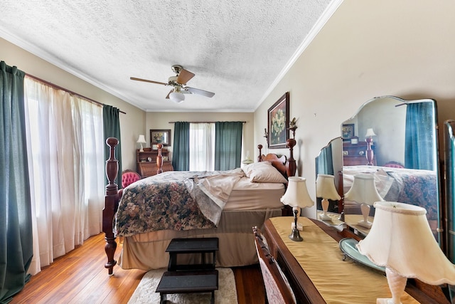 bedroom with light wood-style flooring, a textured ceiling, crown molding, and ceiling fan