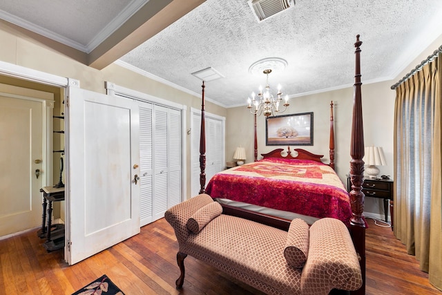 bedroom featuring crown molding, hardwood / wood-style flooring, two closets, a notable chandelier, and visible vents