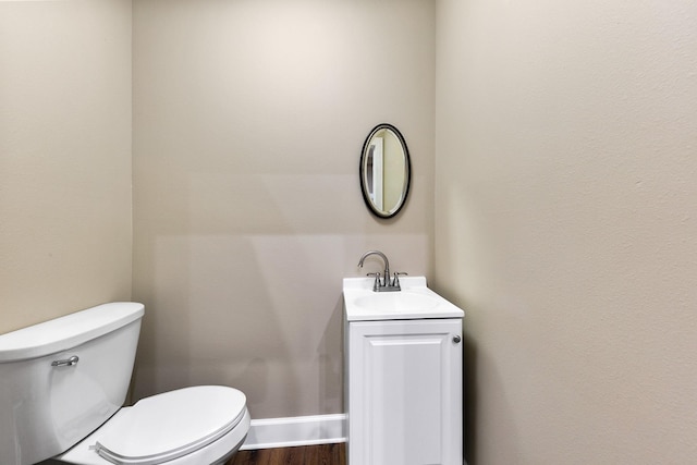 bathroom with toilet, vanity, wood finished floors, and baseboards