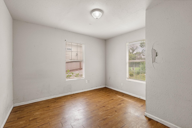 spare room featuring baseboards, a textured wall, and hardwood / wood-style flooring