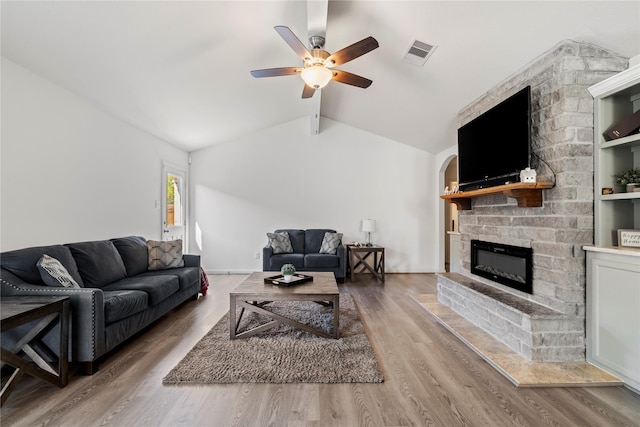 living room with vaulted ceiling with beams, visible vents, a ceiling fan, wood finished floors, and a fireplace