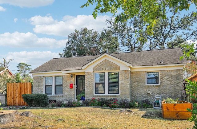 view of front of home featuring roof with shingles, fence, a front lawn, and brick siding