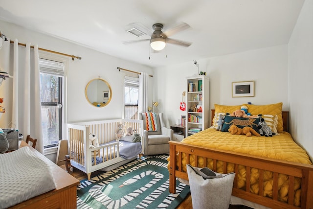 bedroom featuring ceiling fan, visible vents, multiple windows, and wood finished floors