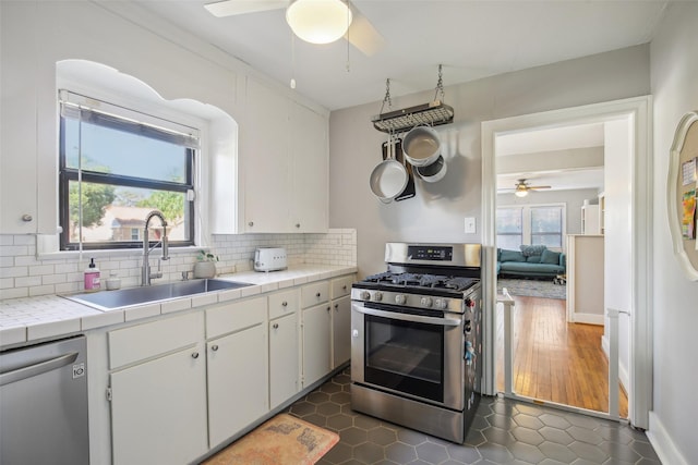 kitchen with white cabinets, a sink, a ceiling fan, tile counters, and stainless steel appliances