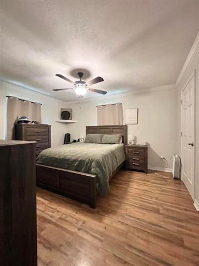 bedroom with light wood-style flooring, a textured ceiling, crown molding, and ceiling fan