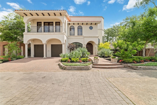 mediterranean / spanish house featuring a garage, stucco siding, a balcony, and decorative driveway