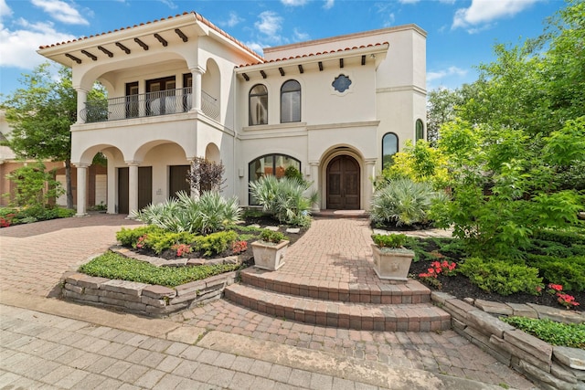 view of front of property featuring a tiled roof, a balcony, stucco siding, an attached garage, and decorative driveway