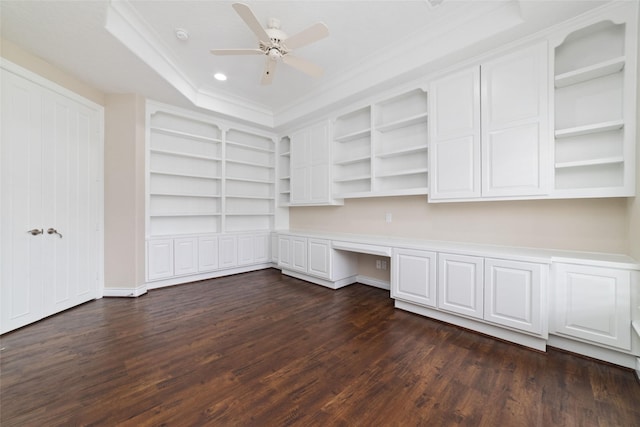 unfurnished office featuring built in desk, a ceiling fan, ornamental molding, dark wood-type flooring, and a raised ceiling
