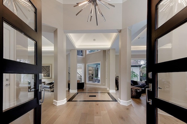 foyer with light wood-style floors, a tray ceiling, baseboards, ornamental molding, and ornate columns