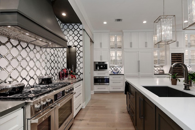 kitchen featuring high end appliances, visible vents, a sink, premium range hood, and decorative backsplash