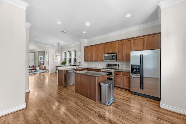 kitchen with stainless steel appliances, ornamental molding, a sink, a kitchen island, and a peninsula