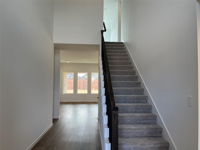 staircase featuring wood finished floors, a towering ceiling, and baseboards