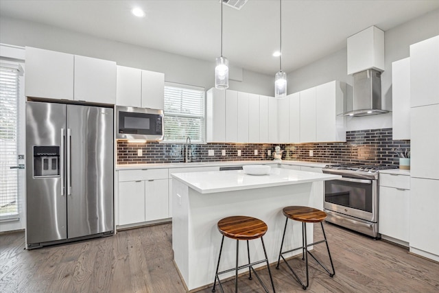 kitchen featuring white cabinets, stainless steel appliances, wall chimney range hood, a sink, and a kitchen bar