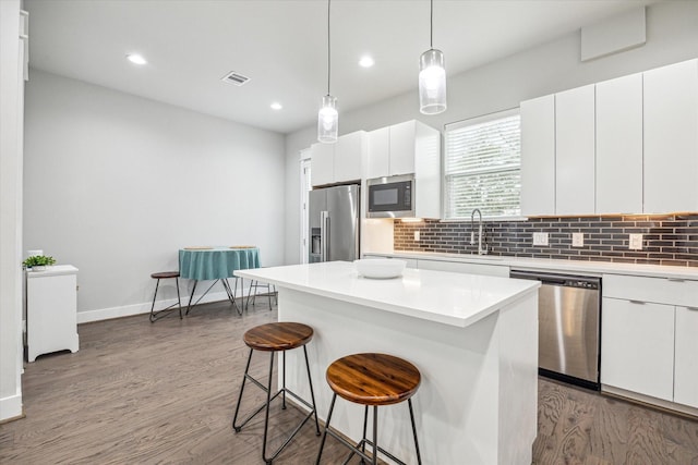 kitchen featuring tasteful backsplash, wood finished floors, stainless steel appliances, a kitchen bar, and visible vents
