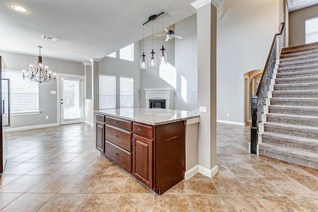 kitchen featuring ornate columns, visible vents, light stone countertops, baseboards, and ceiling fan with notable chandelier