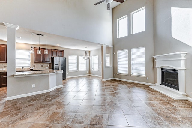 unfurnished living room with ceiling fan with notable chandelier, baseboards, a glass covered fireplace, and a wealth of natural light