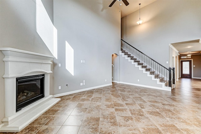unfurnished living room with stairway, ceiling fan, baseboards, and a high ceiling