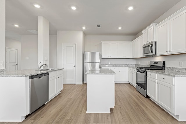 kitchen with appliances with stainless steel finishes, a center island with sink, a sink, light wood finished floors, and white cabinetry