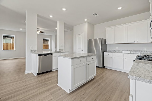 kitchen with stainless steel appliances, light wood-type flooring, a sink, ceiling fan, and a center island